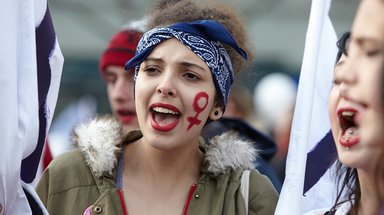 Eine weiblich gelesene Person auf einer Demonstration mit einem roten Frauensymbol auf der linken Wange